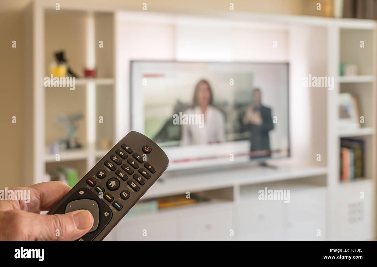 Maschio di mano che tiene il telecomando con TV in background Foto Stock