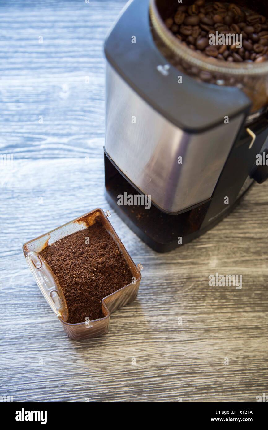 Macchina elettrica per caffè macinacaffè mostra intero Fagioli di la mola con grind su la venatura del legno banco. Foto Stock