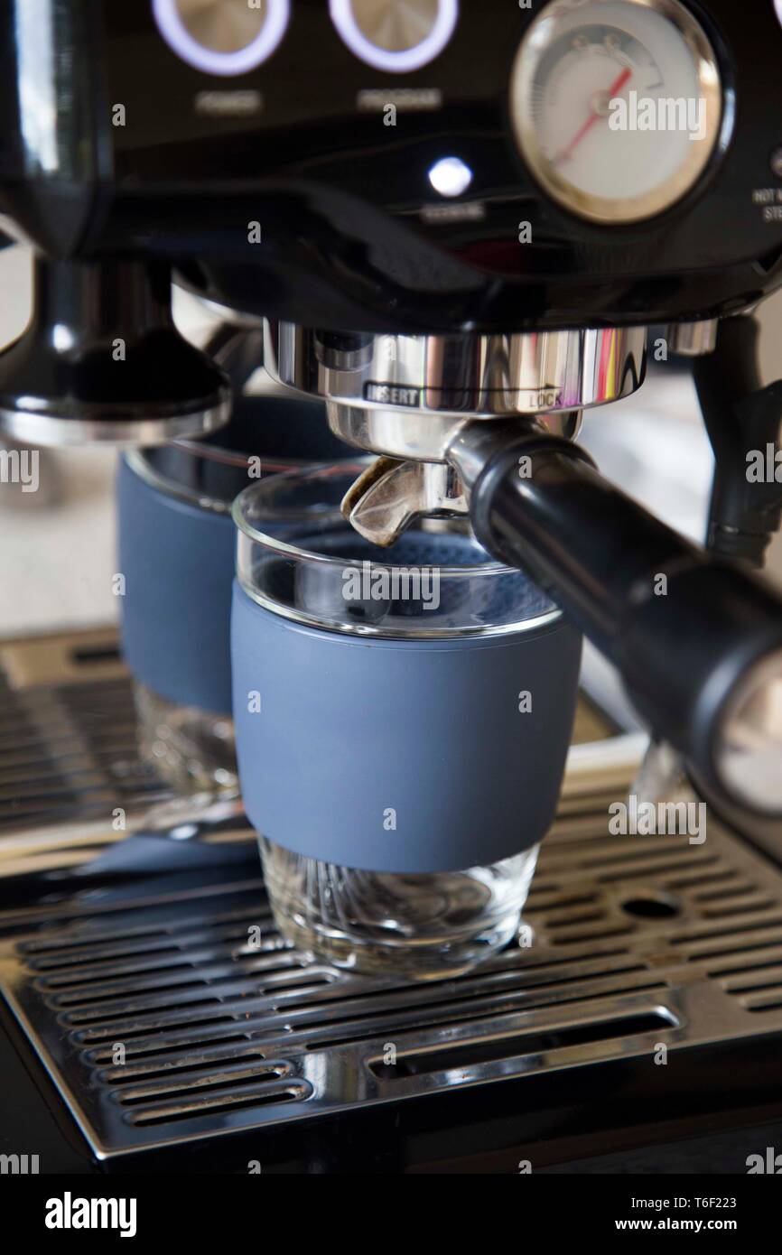 La realizzazione di un caffè espresso a casa in un vetro mantengono cup con manicotto in silicone e coperchio rende un ecologico scelta quando confrontata ad un cafe'. Foto Stock