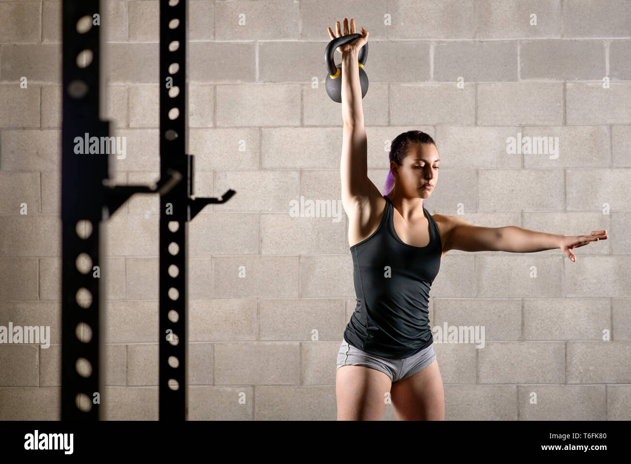 Forte muscolare giovane donna che lavora fuori in una palestra con un peso kettlebell sollevandolo con braccio esteso in una salute e concetto di fitness Foto Stock
