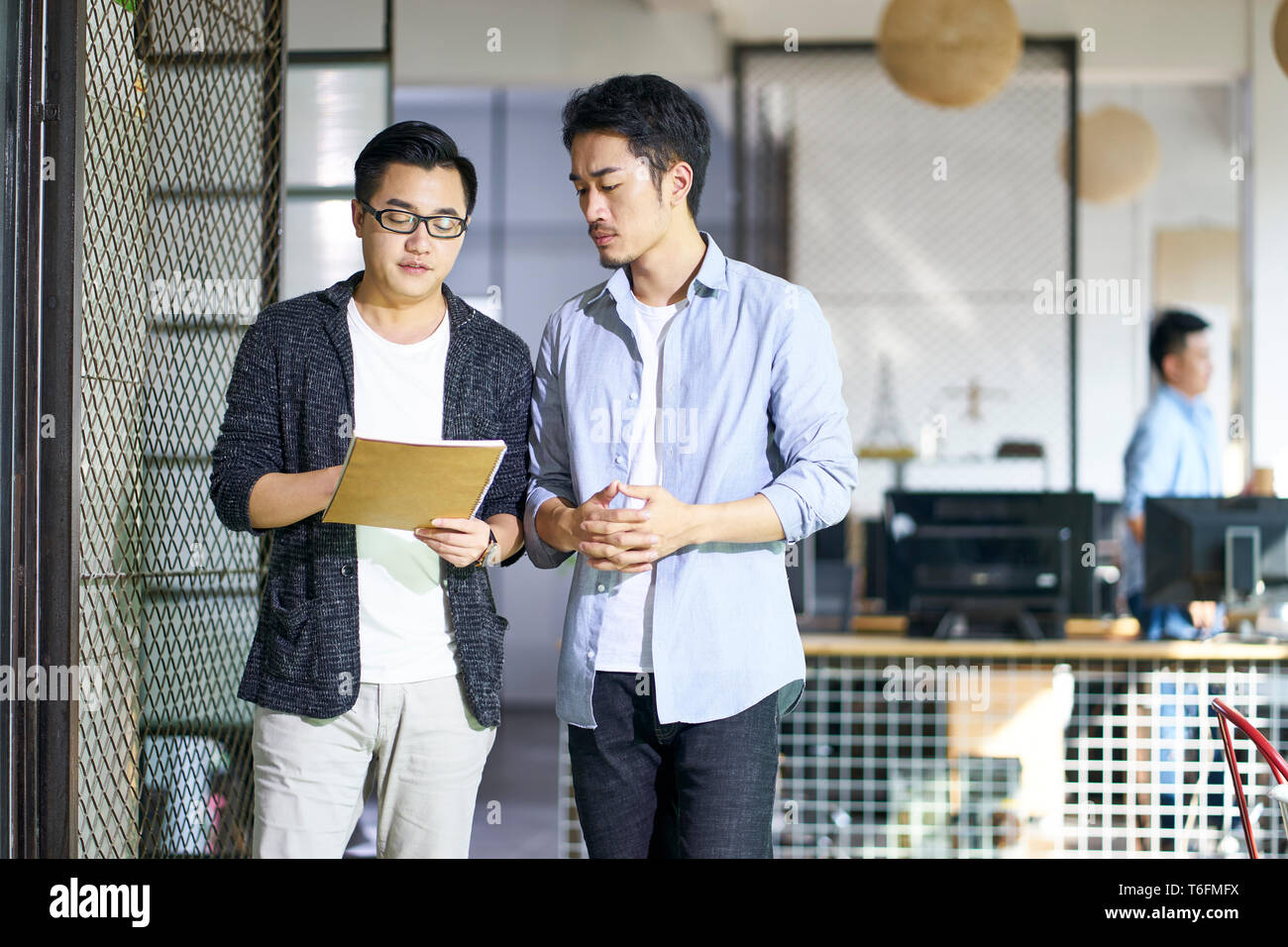 Due giovani colleghi asiatici discutere di affari mentre si cammina in ufficio. Foto Stock
