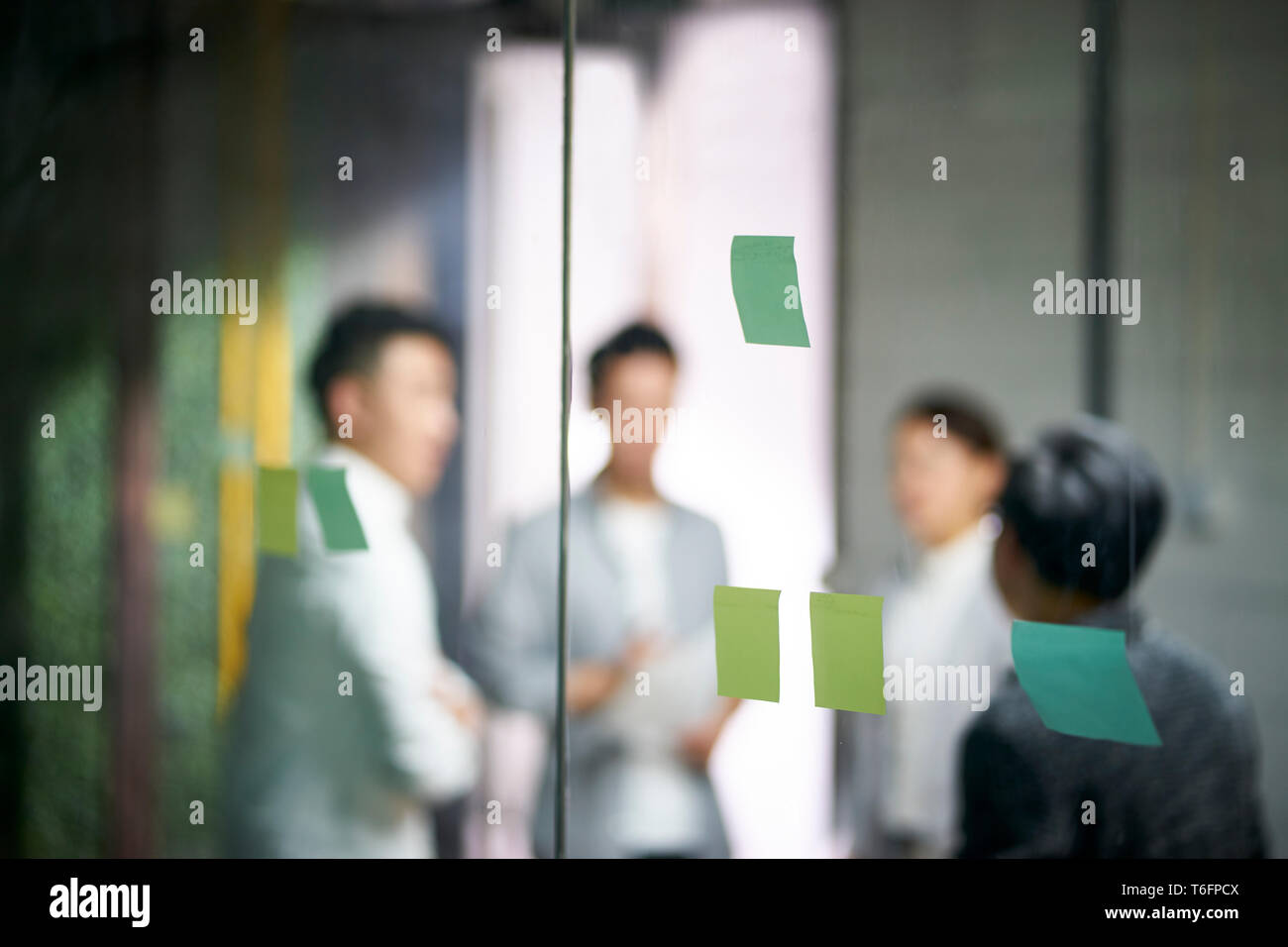 Giovani imprenditori asiatici di piccola impresa a discutere di business plan in office sala riunioni, concentrarsi sulle note di adesivo sul vetro. Foto Stock