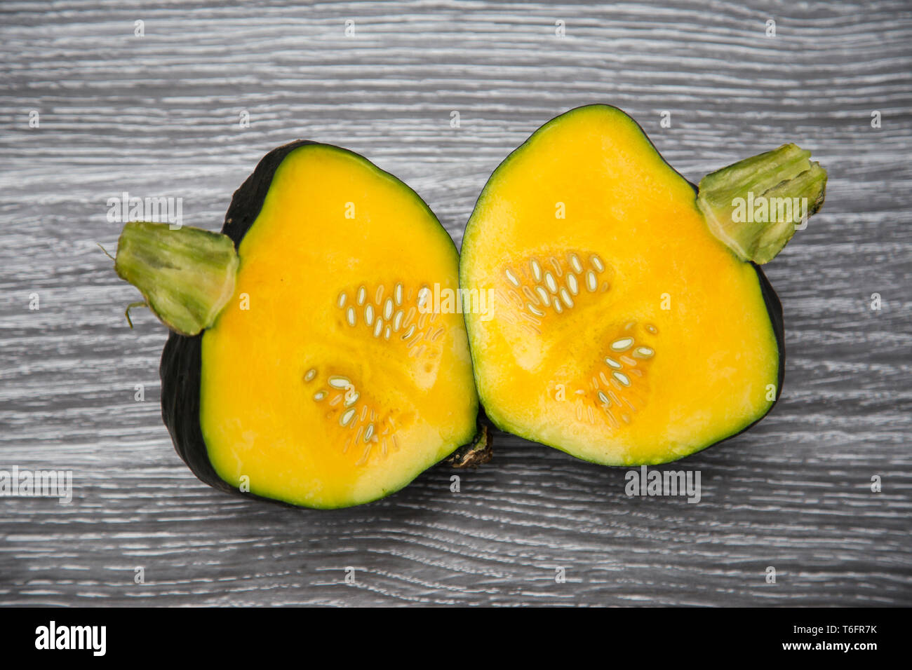 Homegrown ranuncolo organico squash tagliata aperta a metà la posa su una tavola di legno - verde scuro della pelle, luce stelo verde, giallo oro carne e semi. Foto Stock