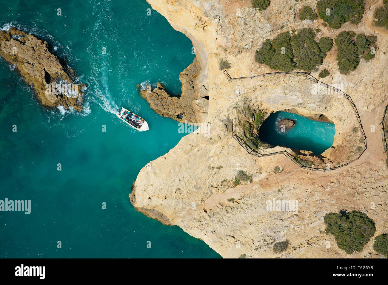 VISTA AEREA. Giro turistico in barca si avvicina a una grotta di mare / buca sul litorale roccioso vicino alla spiaggia di Cão Raivoso. Lagoa, Algarve, Portogallo. Foto Stock