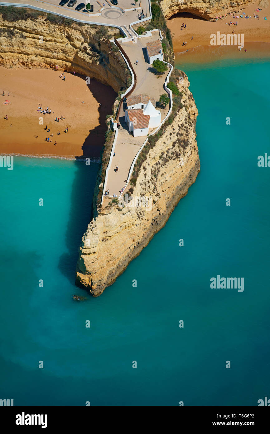VISTA AEREA. Piccola cappella su un promontorio roccioso incredibilmente alto e stretto. Forte di Nossa Senhora da Rocha, Lagoa, Algarve, Portogallo. Foto Stock