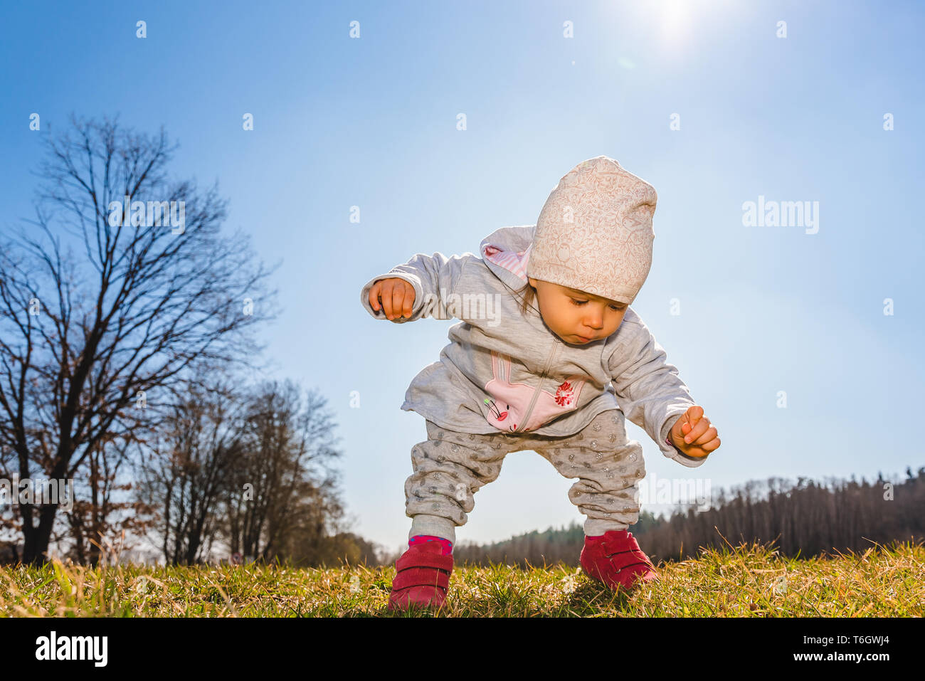 Baby indossare caldo beanie hat, felpa e stivali rossi all'aperto in zona rurale alla scoperta della natura. Molla soleggiato, baby su un prato in pieno sole. Copia spac Foto Stock