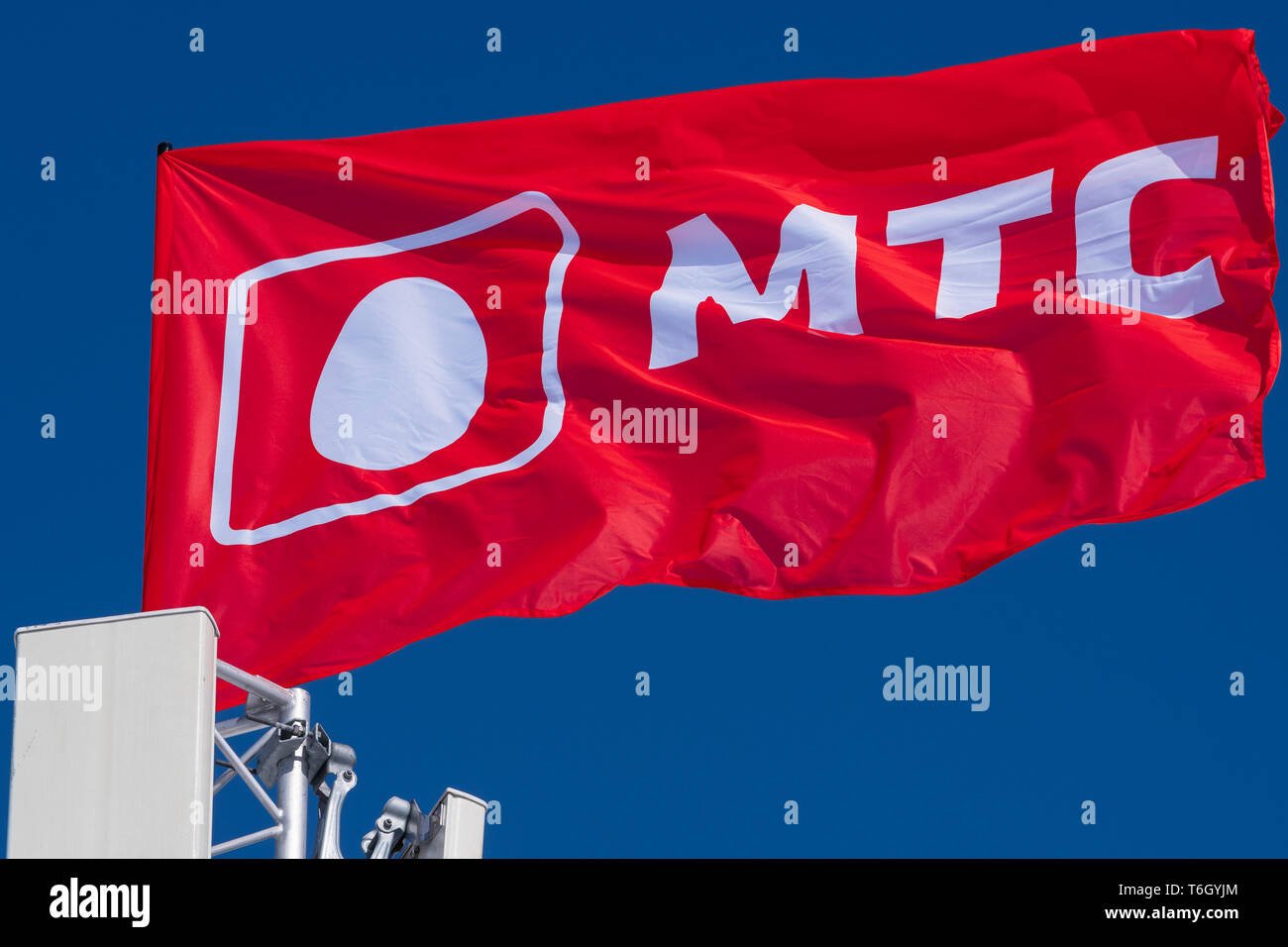 Bandiera con stemma, simboli di Mobile TeleSystems (MTS) - operatore di telefonia mobile nella Federazione russa, CIS. Bandiera sventolare nel vento sullo sfondo azzurro del cielo Foto Stock