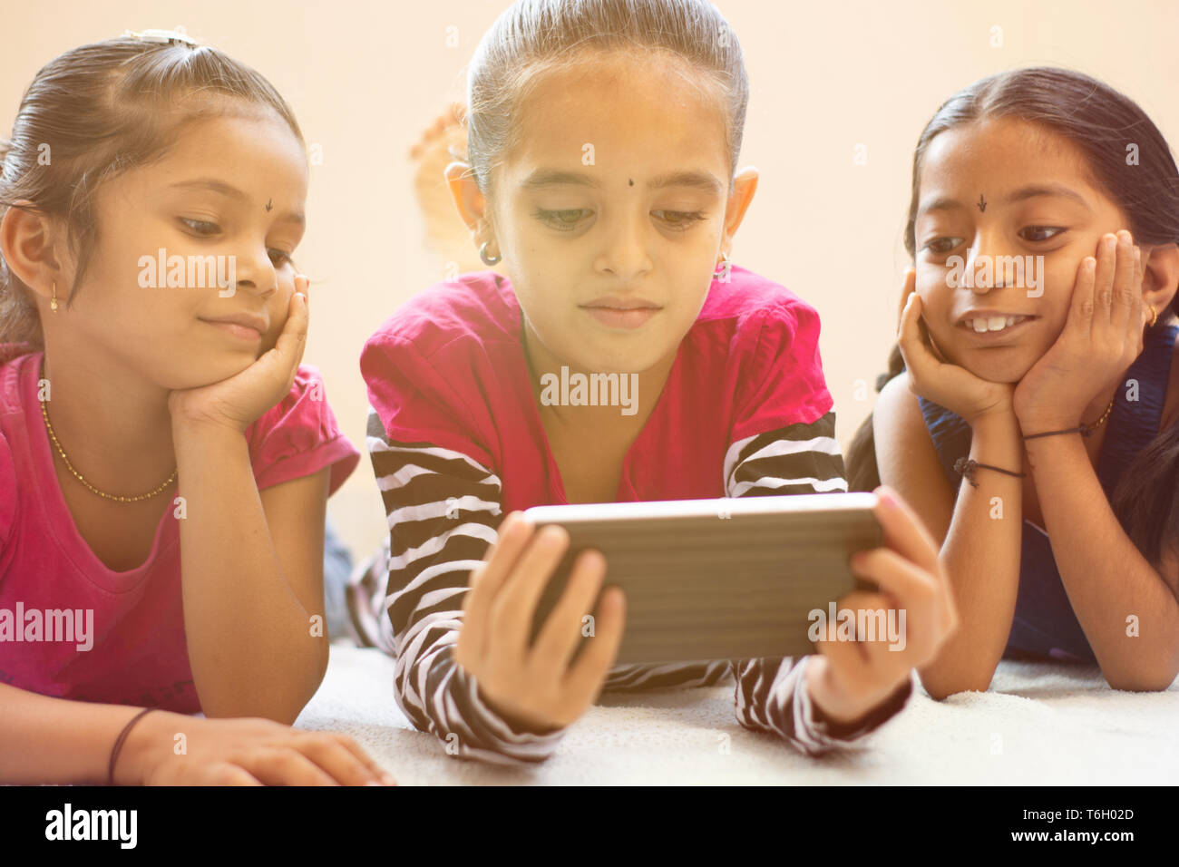 Tre graziosi bambini indiani guardando bambino utilizza lo smartphone con smile sul letto. Foto Stock