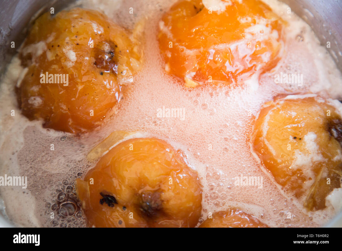 Close up di mele cotogne simmering in un grande vaso in acciaio inossidabile in uno sciroppo di zucchero. Essi hanno trasformato il rosso rubino dai tannini nel frutto. Foto Stock