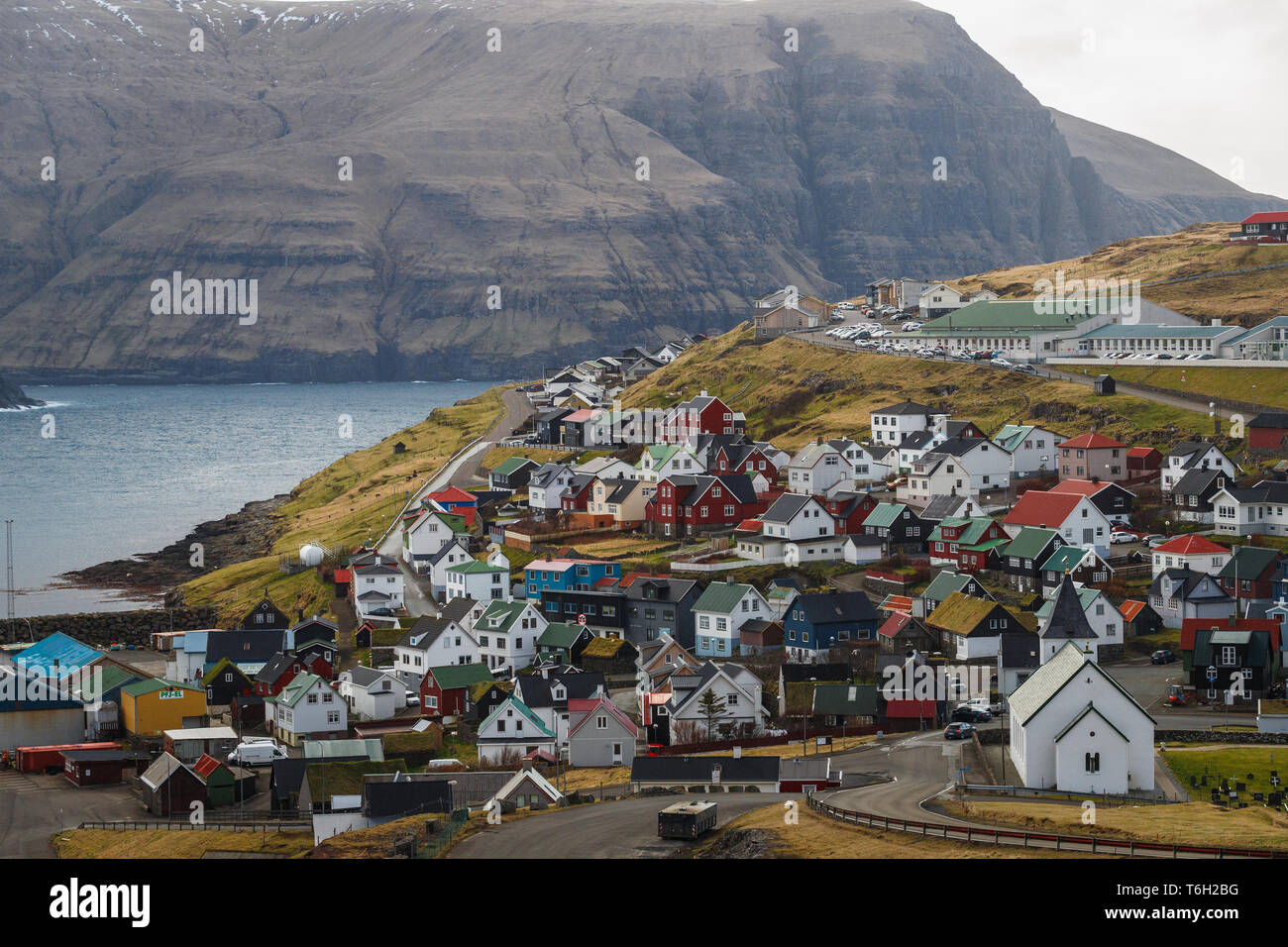 Vista sul villaggio Eiði con le sue case colorate e la chiesa di Eiði davanti a scenic mountain range (Isole Faerøer, Danimarca, Europa) Foto Stock