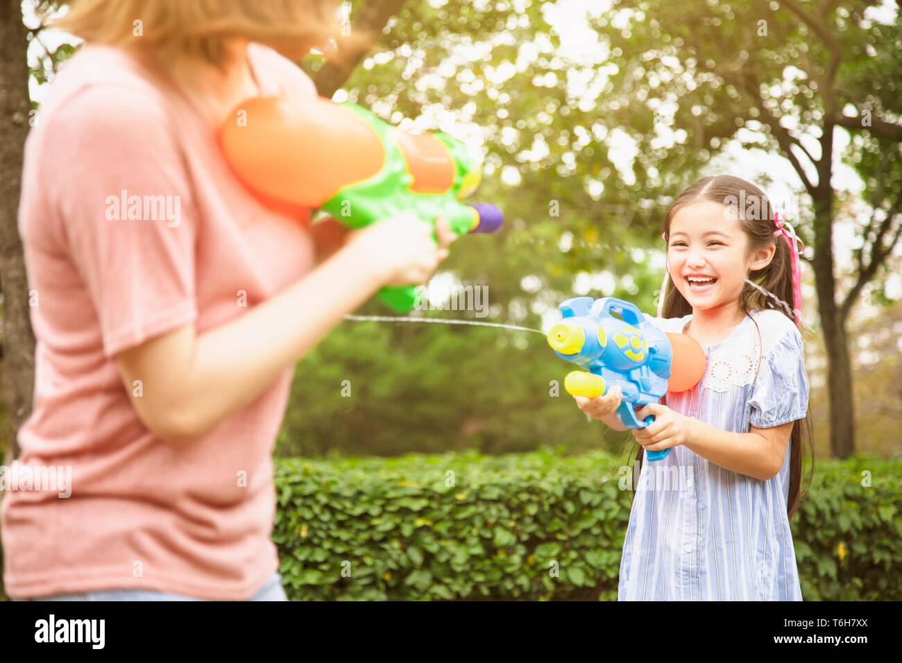 Madre e bambine giocando pistole acqua nel parco Foto Stock