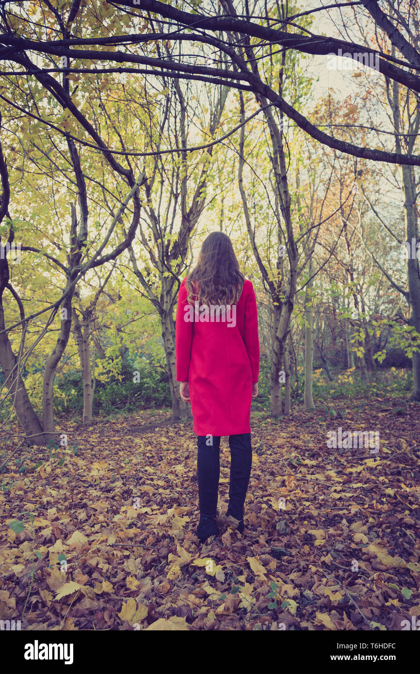 Donna tutta sola nella foresta con un lungo cappotto rosso, rivolto lontano Foto Stock