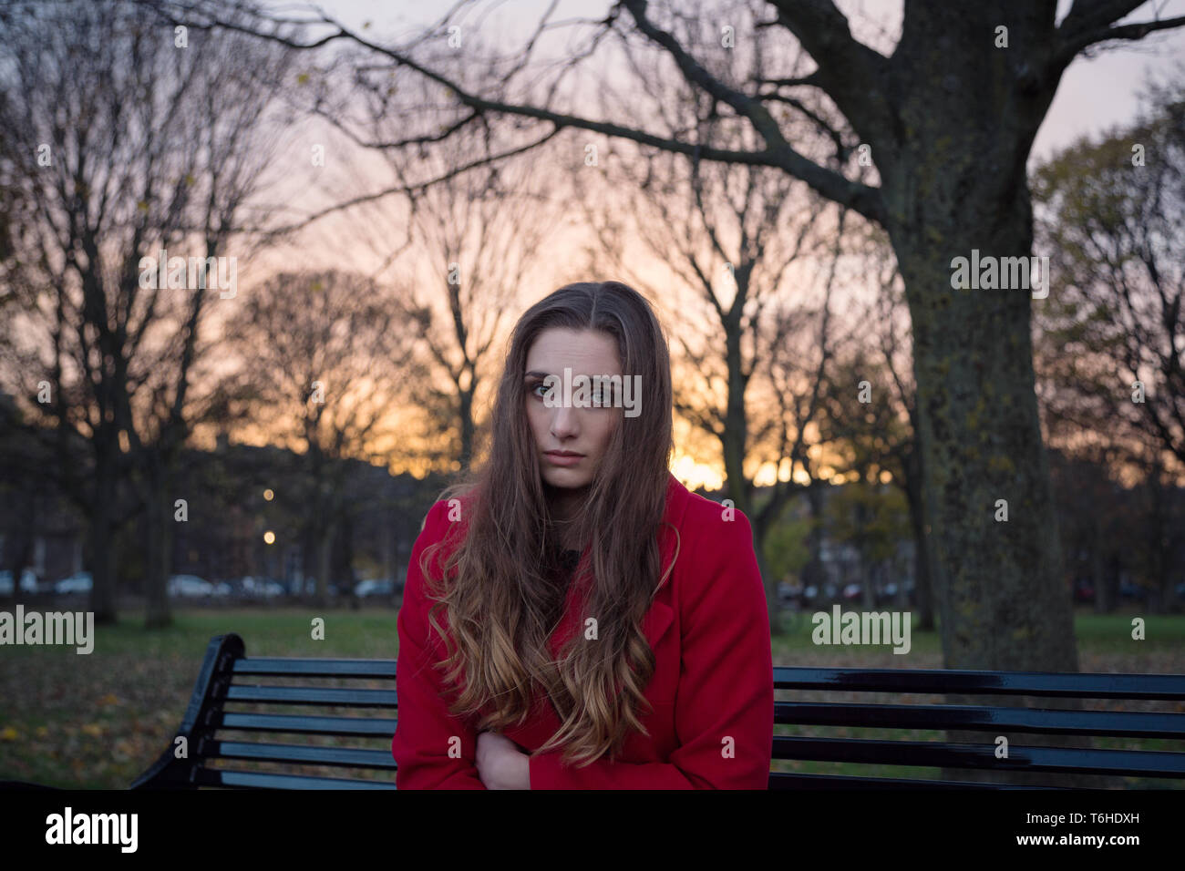 Una giovane donna seduta su una panchina in un parco con un sacco sulla sua mente, sentirsi isolati e ansiosi. Foto Stock