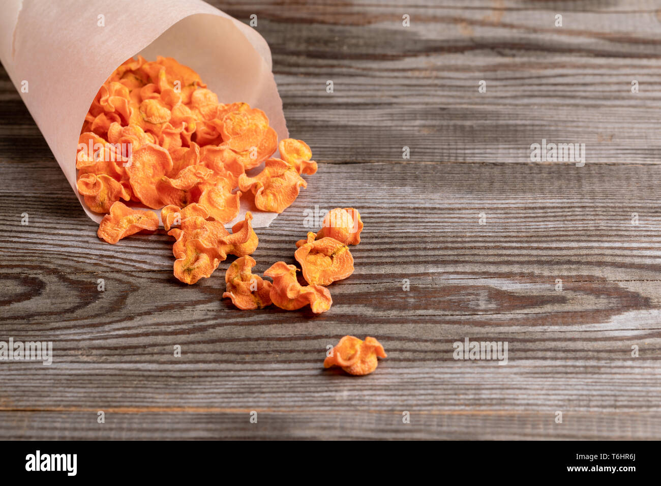 Orange piccola carota chips caduta dal libro bianco borsa per il vecchio tavolo in legno. Foto Stock