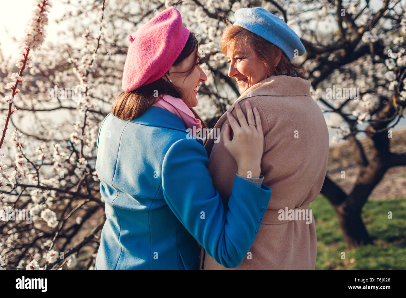 Felice senior madre e figlia abbracciando in primavera in fiore giardino al tramonto. La festa della mamma concetto. I valori della famiglia Foto Stock