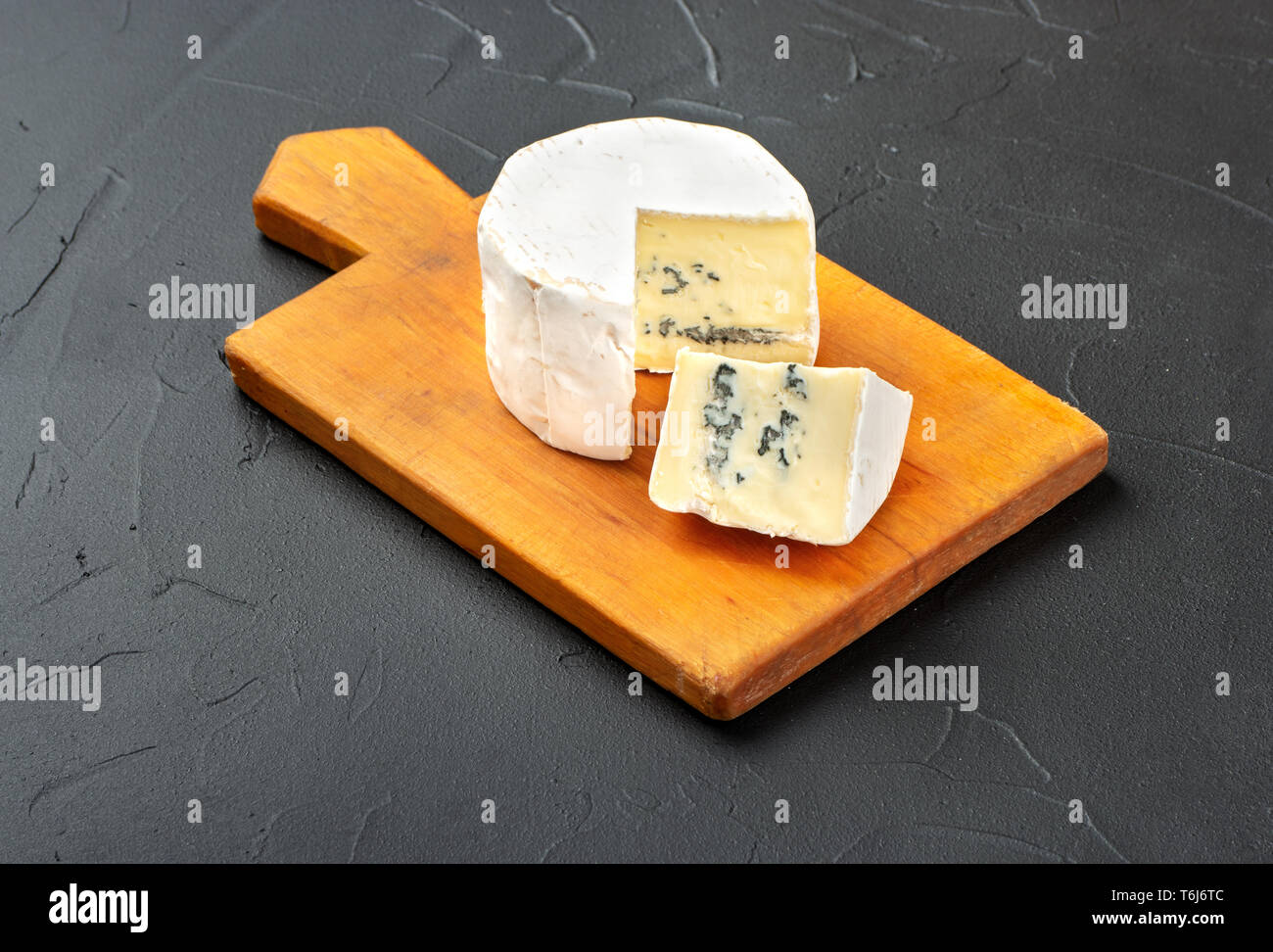 Formaggio Brie con fetta sul tagliere e scuro dello sfondo in calcestruzzo Foto Stock