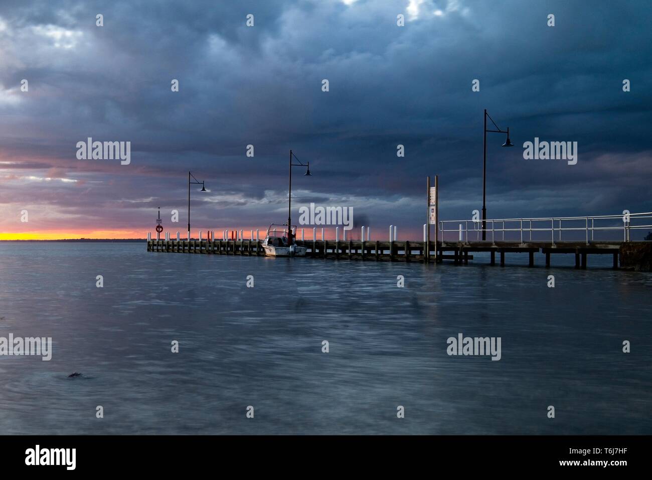 Piccola barca bianca ormeggiata al lago re Jetty in Metung sotto un meditabondo rosa e grigio cielo al tramonto Foto Stock