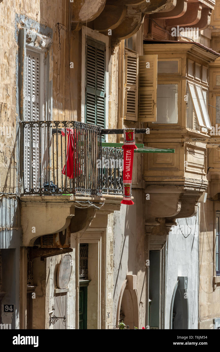 Un rosso brillante Valletta football club sciarpa pende dal balcone di una tradizionale casa in pietra di La Valletta Foto Stock
