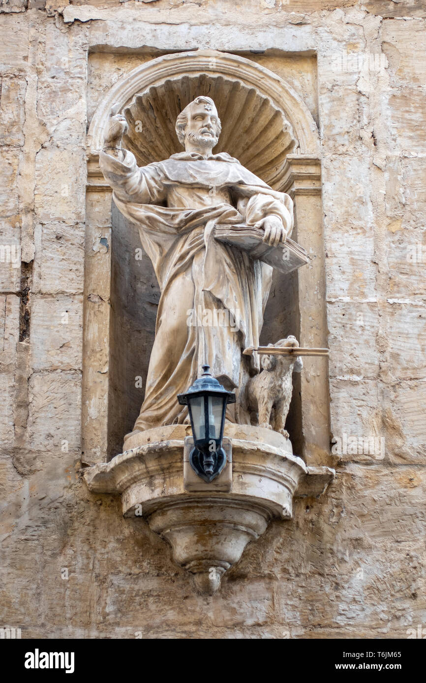 La statua scolpita la statua di San Domenico con la sua porta torcia cane, in una nicchia di una parete in St Nicholas Street a La Valletta, Malta Foto Stock