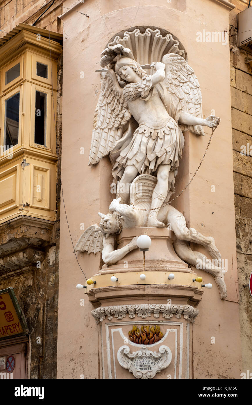 Una statua di San Michele Arcangelo di calpestare Satana in piedi su un basamento in corrispondenza della zona di spigolo di Sant'Orsola e l Arcivescovo le strade de La Valletta. Foto Stock