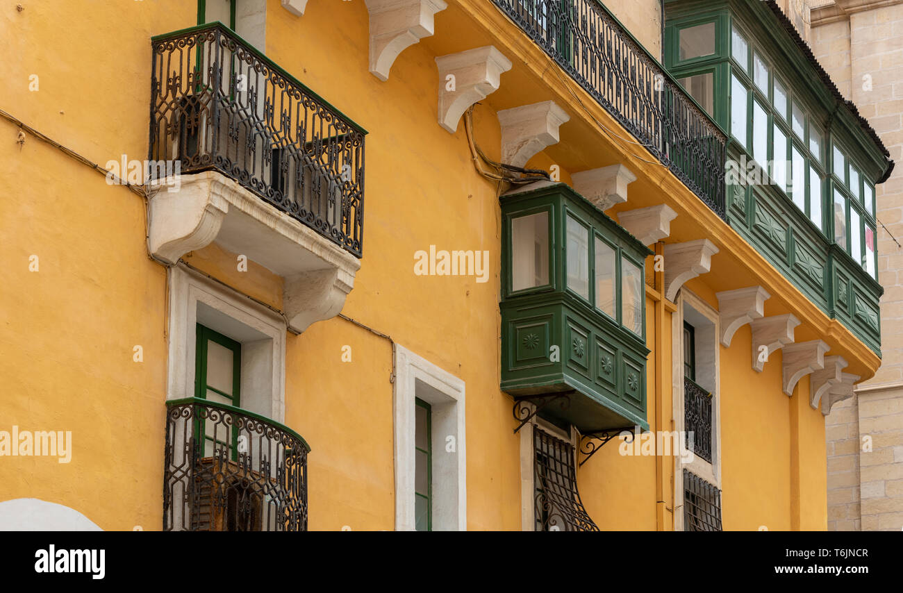 Racchiuso in legno e aprire i balconi in ferro battuto decorano questo luminoso edificio color ocra su un angolo della repubblica e St Christopher strade di La Valletta Foto Stock