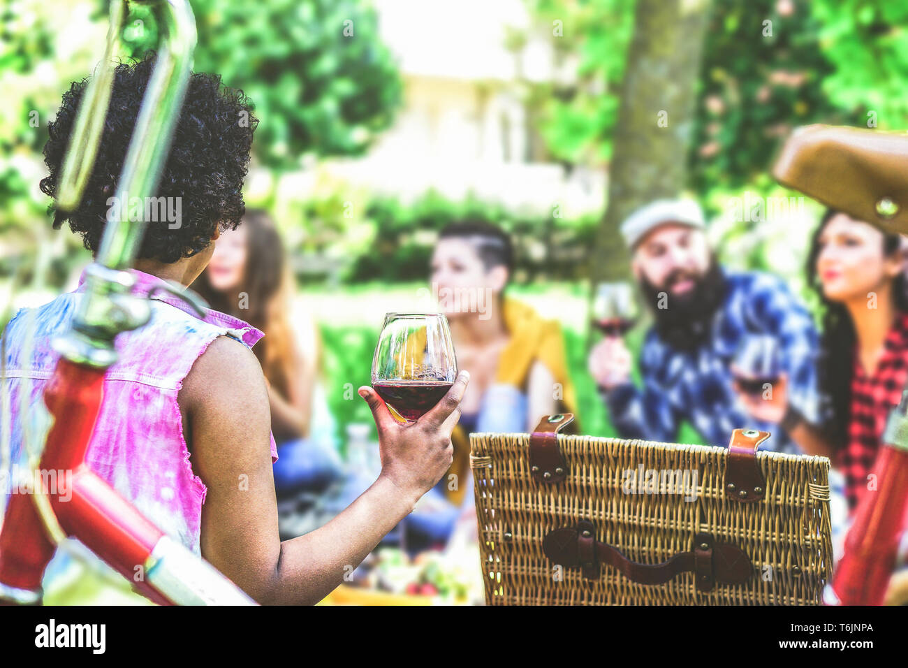 Gruppo di amici facendo un pic-nic in un giardino all'aperto - Happy giovani aventi un divertente incontro con cibo e vino rosso seduto sul prato in un parco Foto Stock