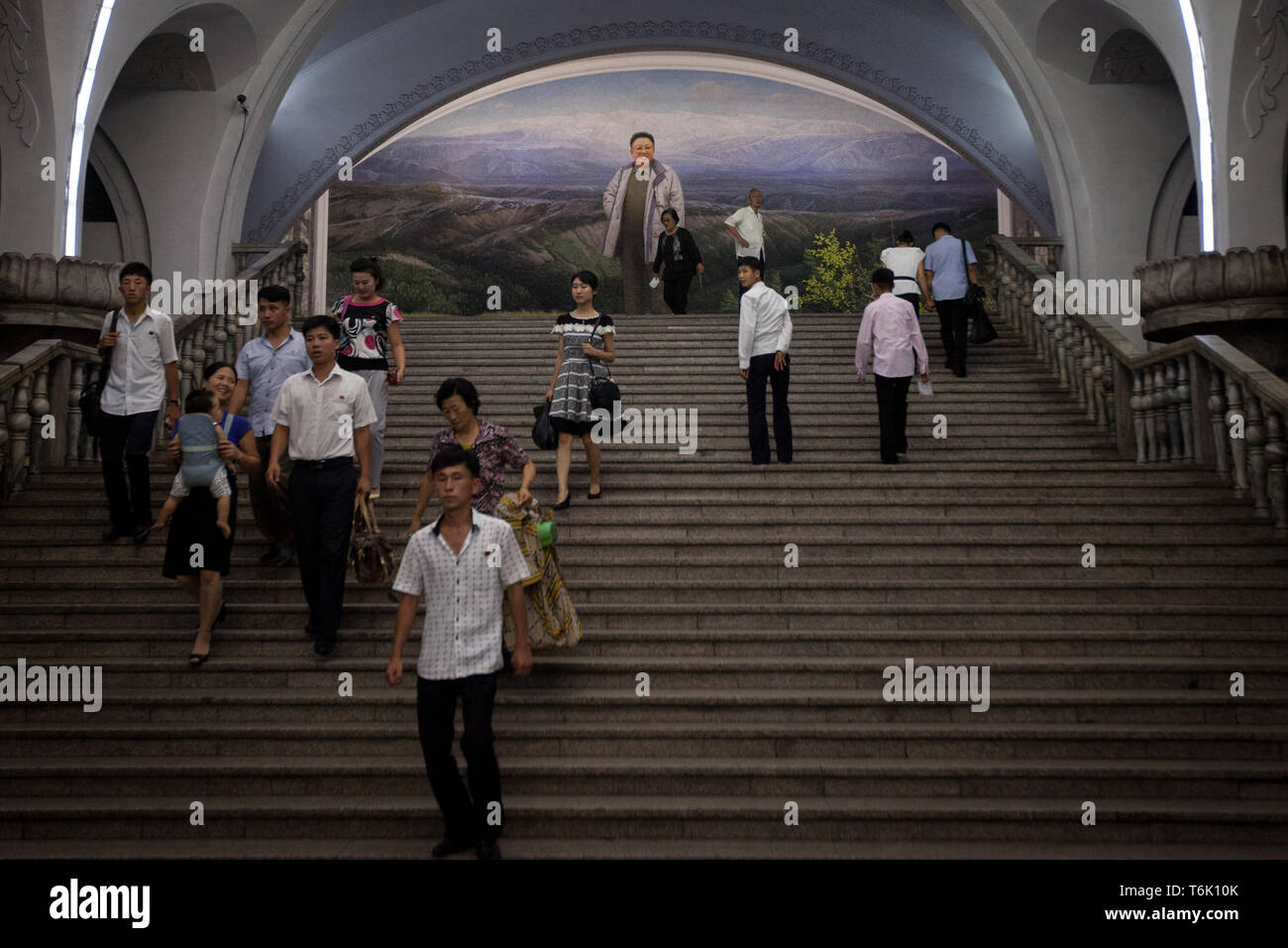 I passeggeri sulla metropolitana di Pyongyang a piedi sotto un grande murale raffigurante Kim Il Sung. Foto Stock