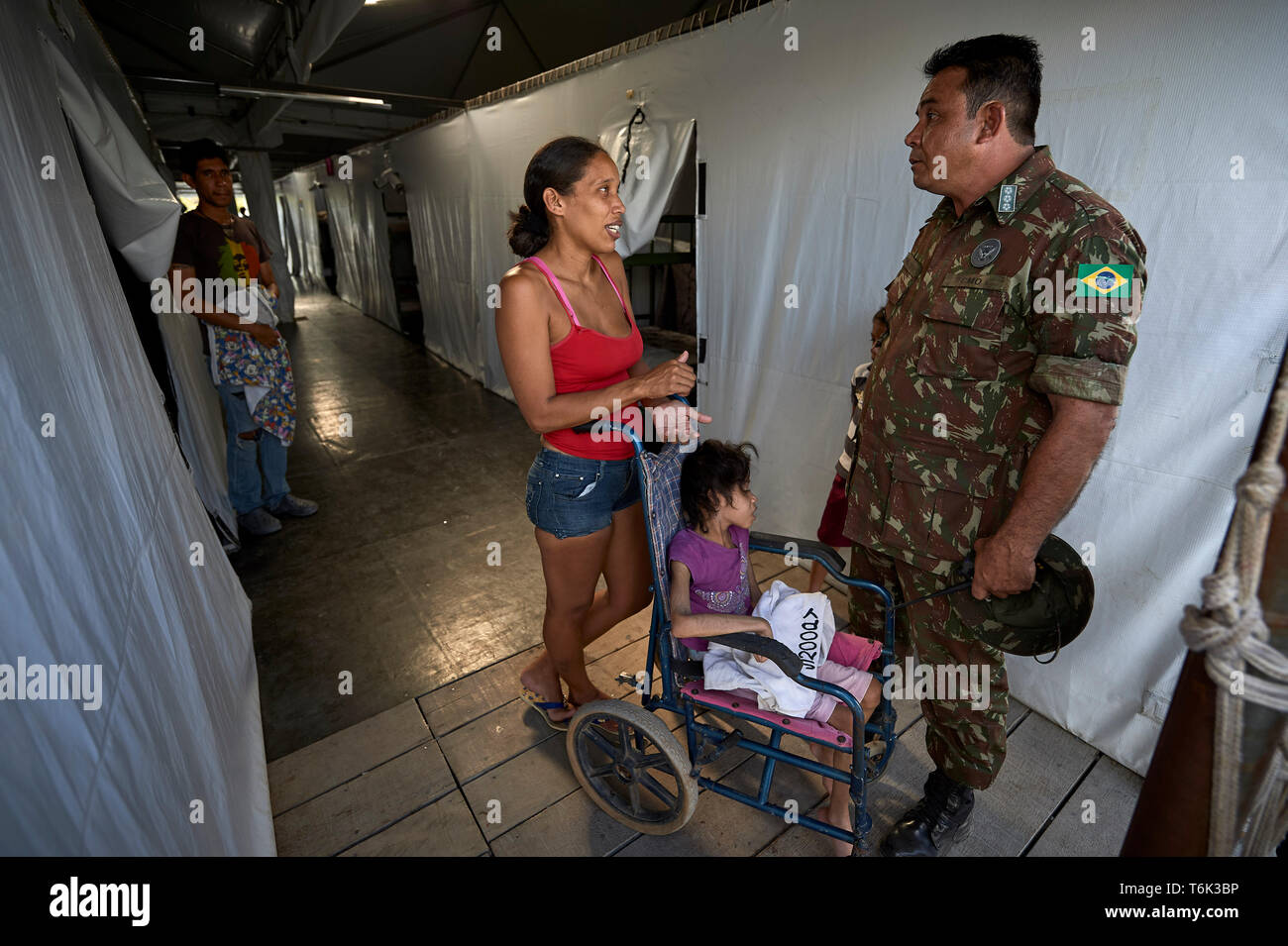 Col. Antonio Vamilton Lopez de Franca Filho colloqui con Yesenia Huarique, la cui figlia è in una sedia a rotelle, in un campo di rifugiati in corrispondenza di Pacaraima, Brasile. Foto Stock