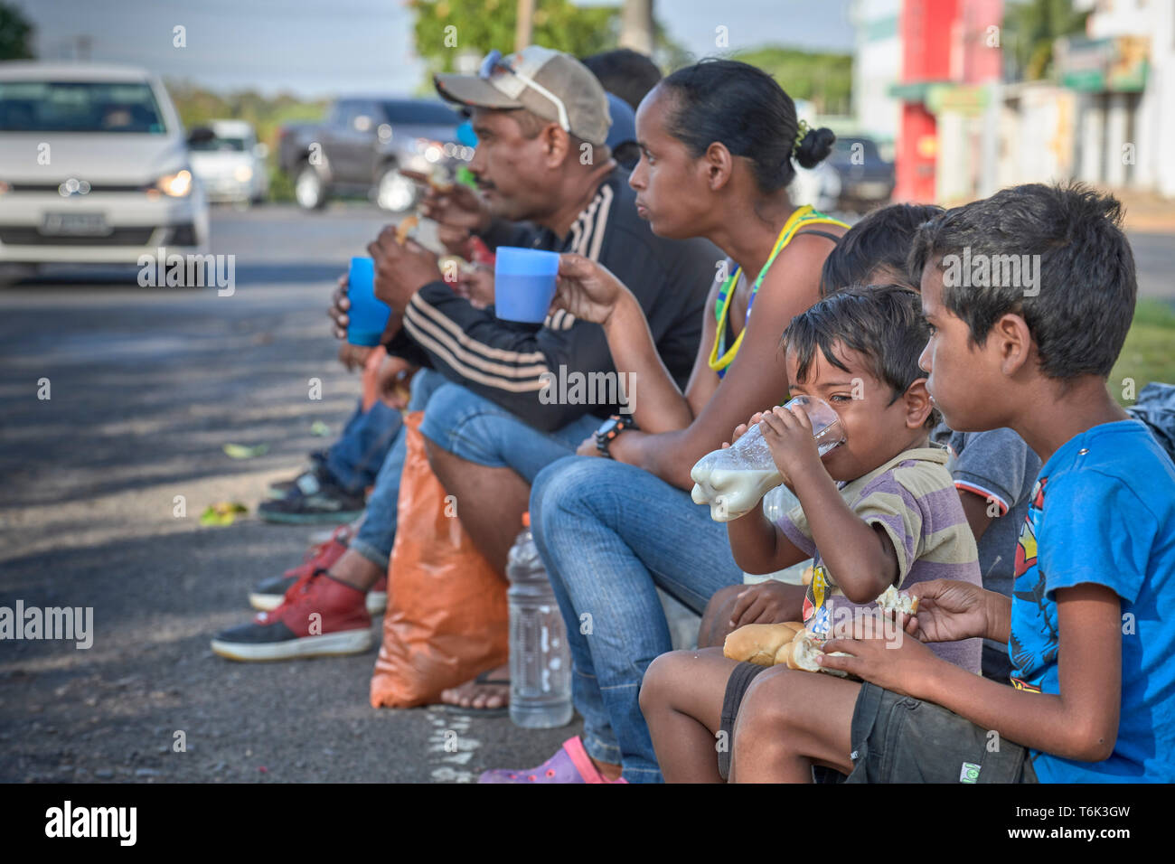 Rifugiati venezuelano di sedersi su un cordolo in Boa Vista, Brasile, mangiare la colazione fornita da Sorelle Missionarie della Consolata. Foto Stock