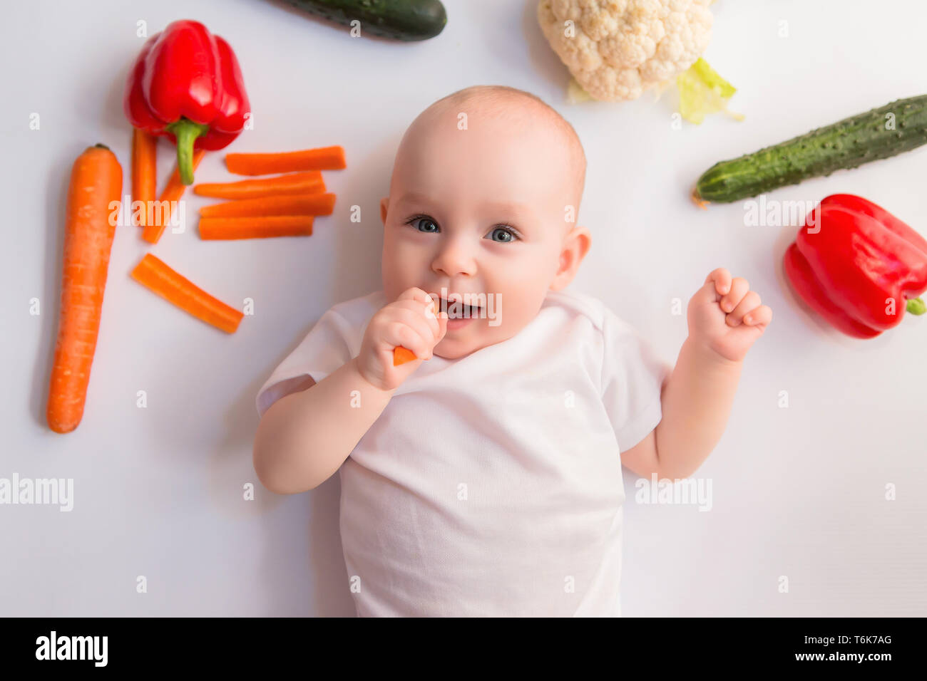 Una sana nutrizione infantile, cibo sfondo, vista dall'alto. Sorridente baby 8 mesi circondato con differenti di frutta fresca e verdura su bianco backgroun Foto Stock