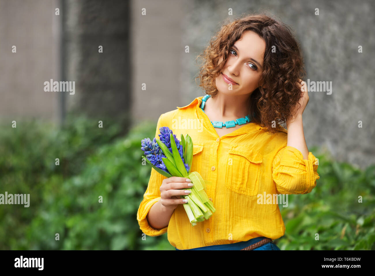 Felice moda giovane donna con bouquet di fiori a piedi nella città strada elegante modello femminile indossare magliette di colore giallo e la gonna blu Foto Stock