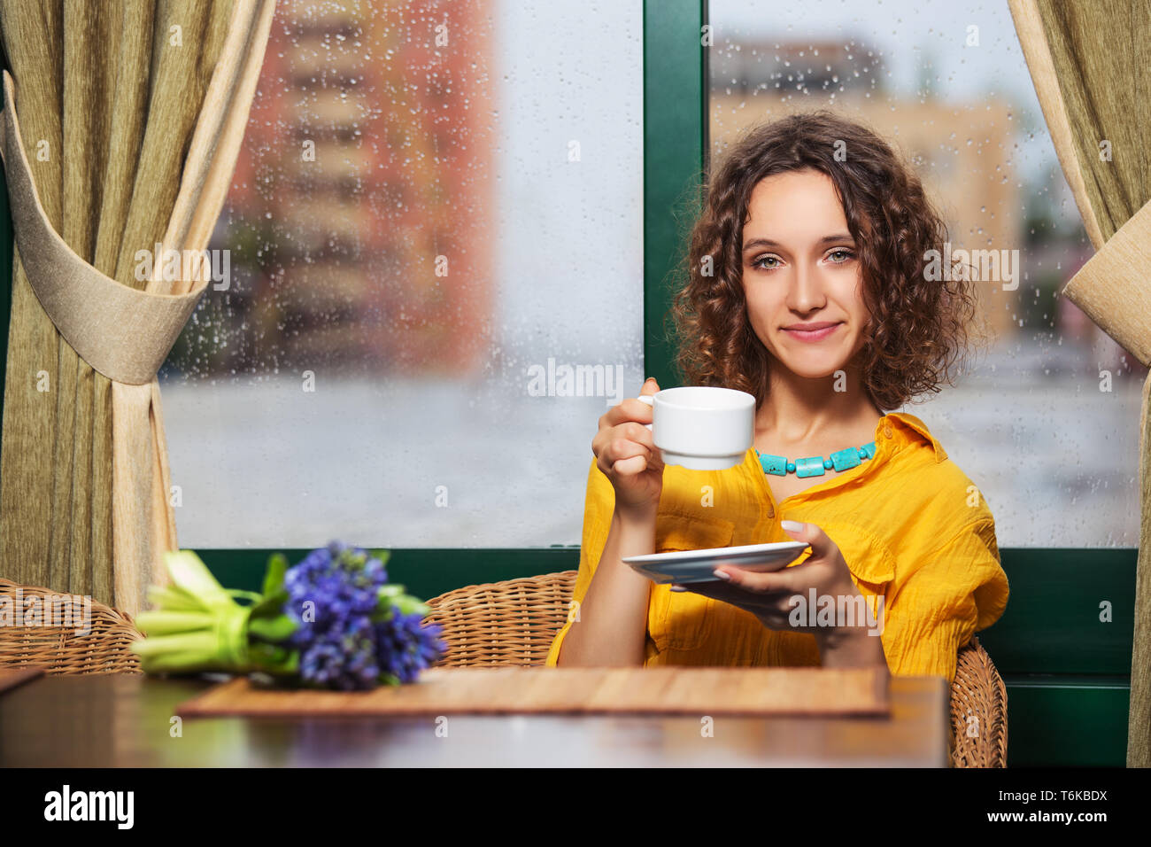 Moda giovane donna bere il tè al ristorante elegante modello femmina marrone con capelli ricci in maglietta gialla Foto Stock