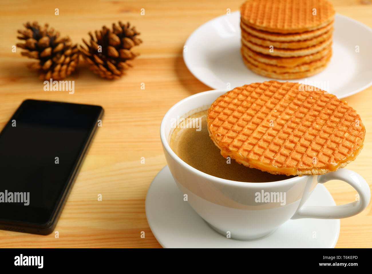 Uno Stroopwafel posto sulla tazza di caffè e una piastra della sua pila in background con un cellulare e secco coni di pino Foto Stock