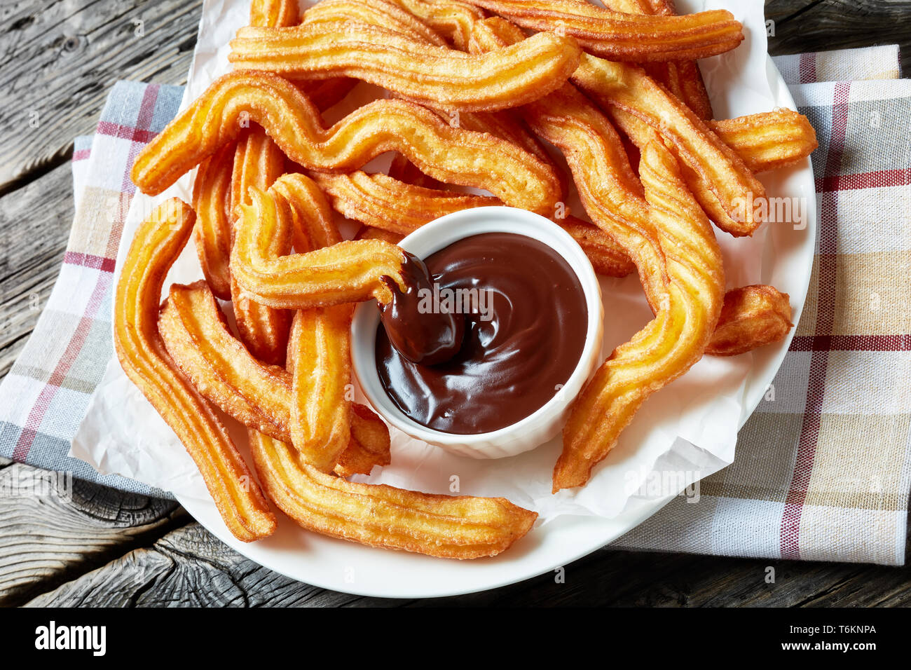 Close-up di churros - tradizionale Spagnola e Messicana dessert su una piastra bianca con cioccolato immersione su di un tavolo di legno con tovagliolo, vista orizzontale f Foto Stock
