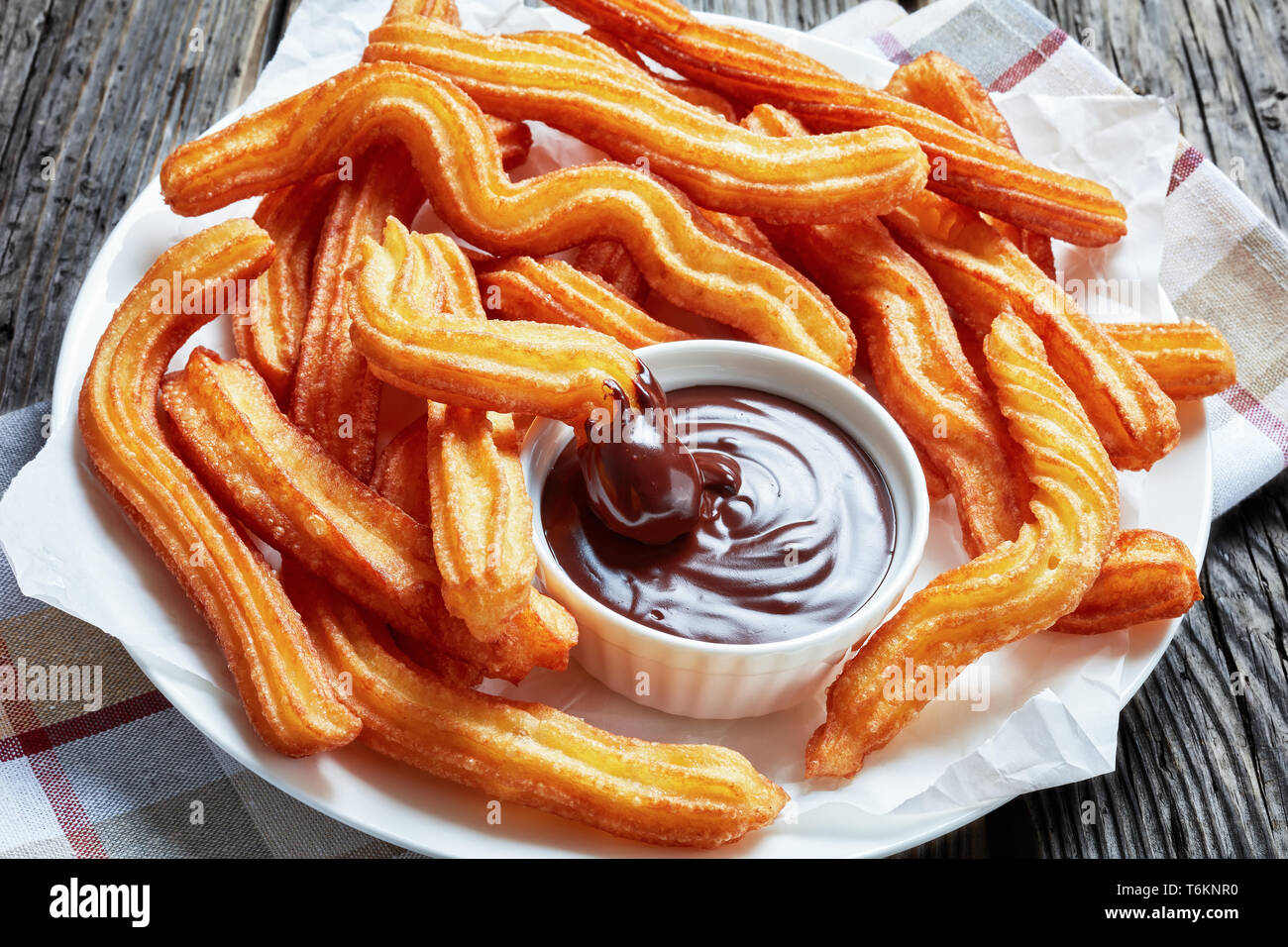 Deliziosi fritti churros servita con cioccolato immersione su una piastra bianca su una tavola di legno con tovagliolo, tradizionale spagnola e messicana street food Foto Stock