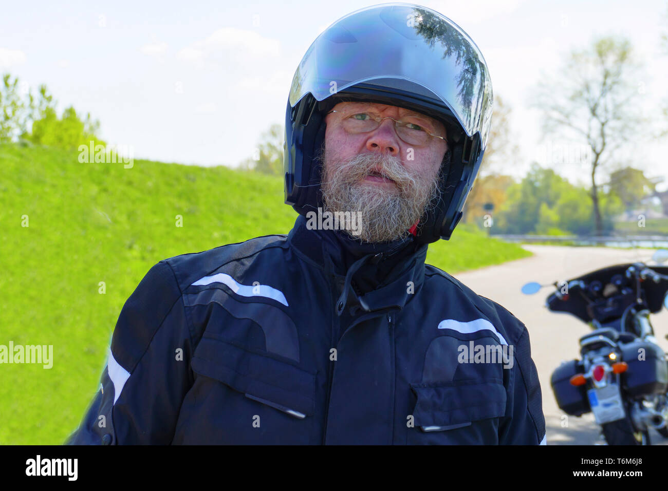 Mann mit langem Bart, Brille und Motorradhelm, steht am Ufer des Rhein Foto Stock