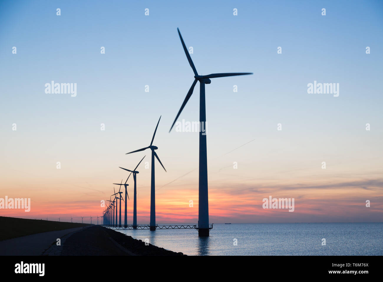 Lunga fila di windturbines con il tramonto sul mare Foto Stock