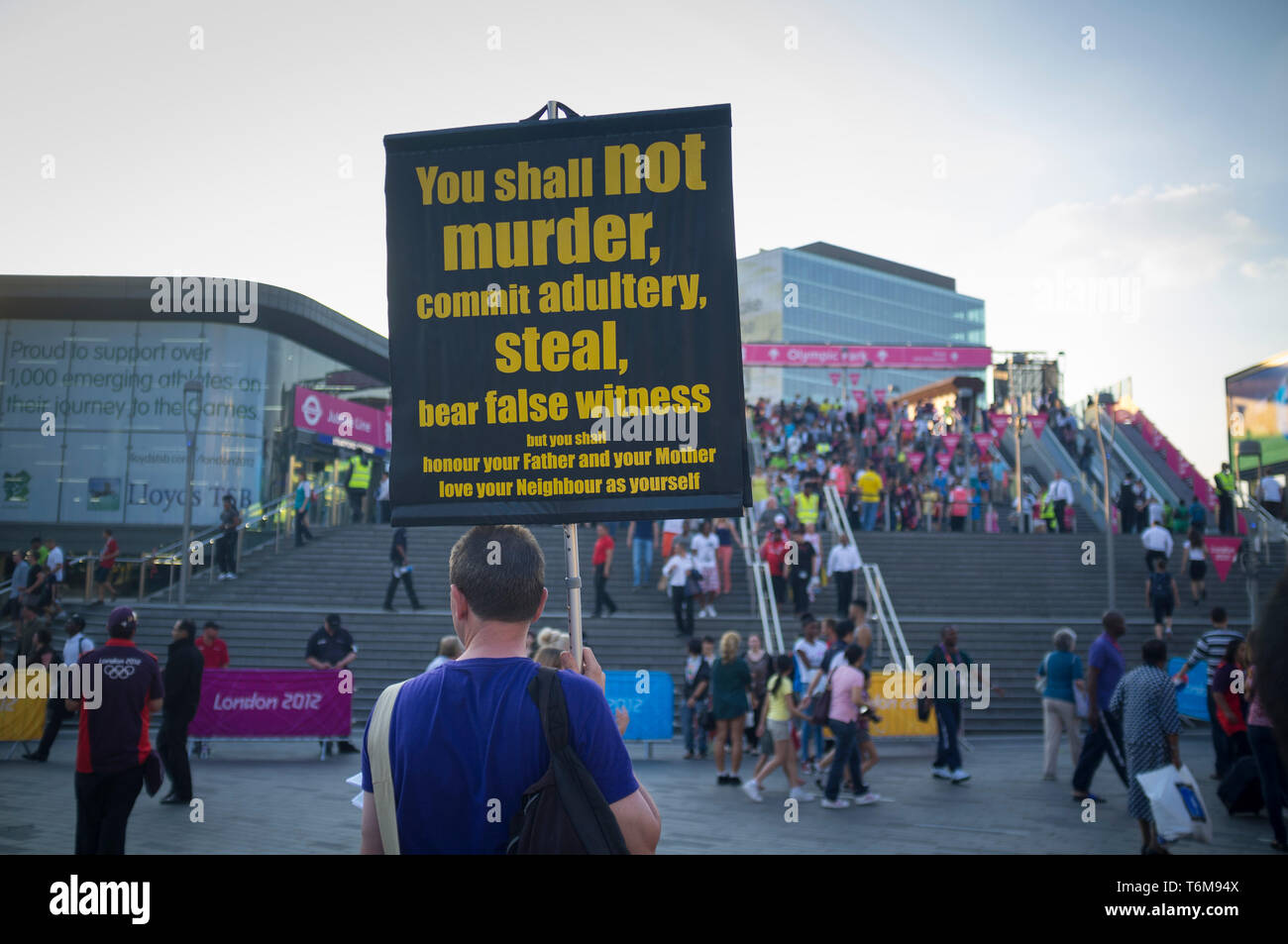 Un uomo detiene un banner religiosa al di fuori la stazione di Stratford per le Olimpiadi di Londra 2012 che mostra alcuni dei dieci comandamenti Foto Stock