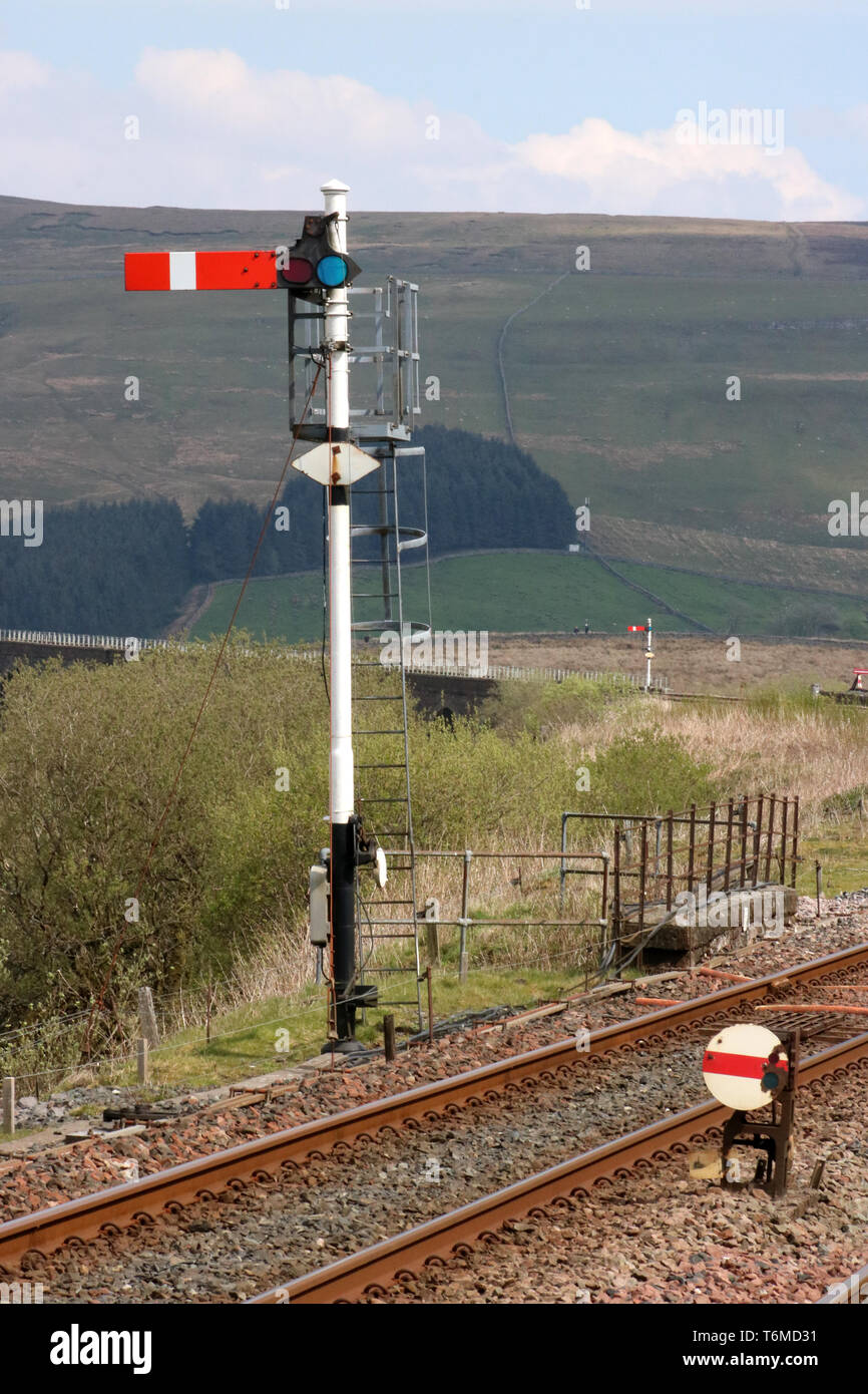 Vista nord est lungo la via verso un semaforo il segnale ferroviario e il segnale di massa dalla via visto dalla stazione Garsdale a stabilirsi a Carlisle linea. Foto Stock