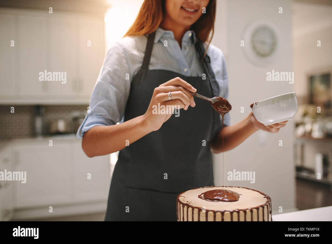 Donna di colata di cioccolato liquido sulla torta per decorare. Lo chef femmina preparazione gustosa torta al cioccolato in cucina. Foto Stock