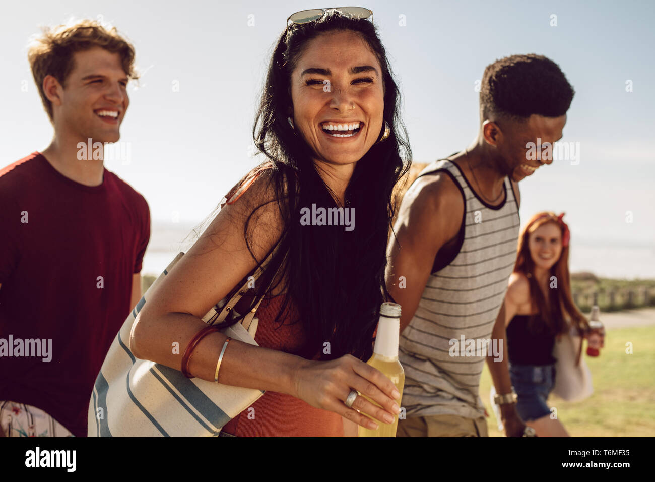 Allegro giovane donna in possesso di una bottiglia di birra passeggiate all'aria aperta con gli amici. Gli amici di andare in spiaggia con bevande su un giorno d'estate. Foto Stock