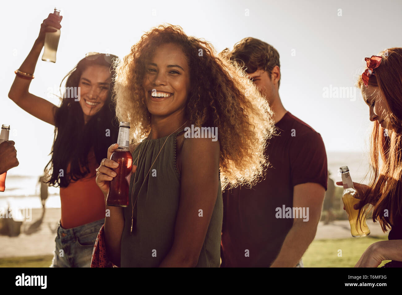 Allegro giovane donna tenendo la birra ballando con i suoi amici all'esterno. Femmina godendo le vacanze estive con gli amici. Foto Stock