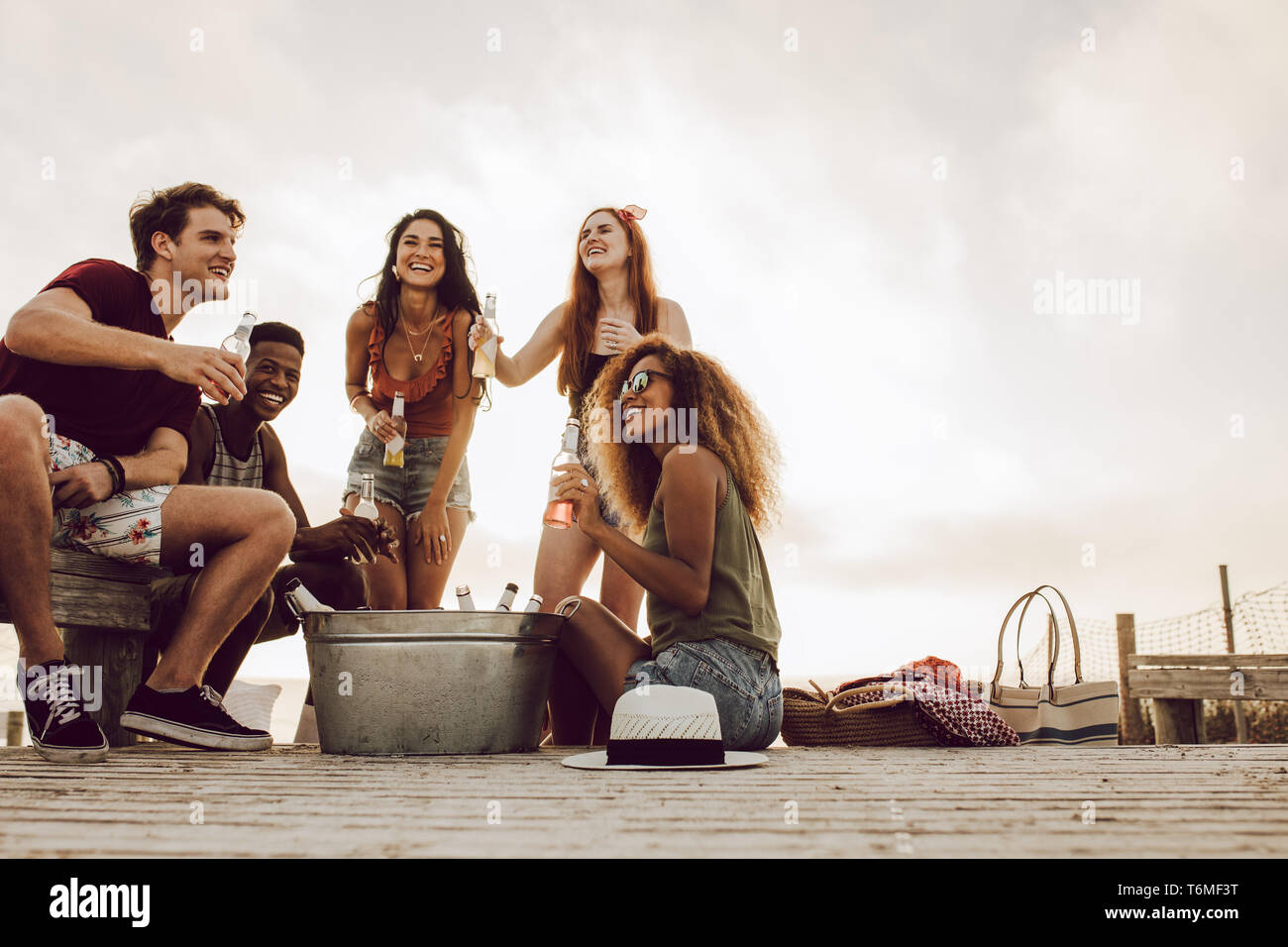 Un gruppo di uomini e donne seduti in spiaggia con birre. Cinque giovani amici festa sulla spiaggia. Foto Stock
