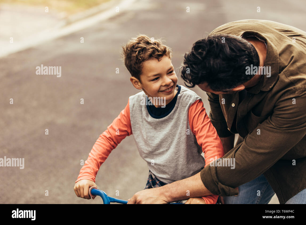 Padre di istruire il suo figlio su una bicicletta. L'uomo aiutando il suo figlio per imparare ad andare in bicicletta. Foto Stock