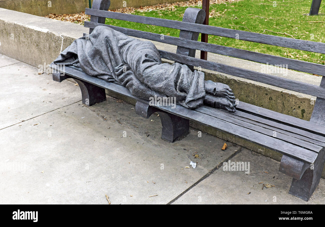 La statua di Gesù Senza Dimora di dimensioni reali, situata su una panchina del parco, è una scultura di Tim Schmalz situata fuori da una cattedrale di Pearl Street a Buffalo, New York. Foto Stock
