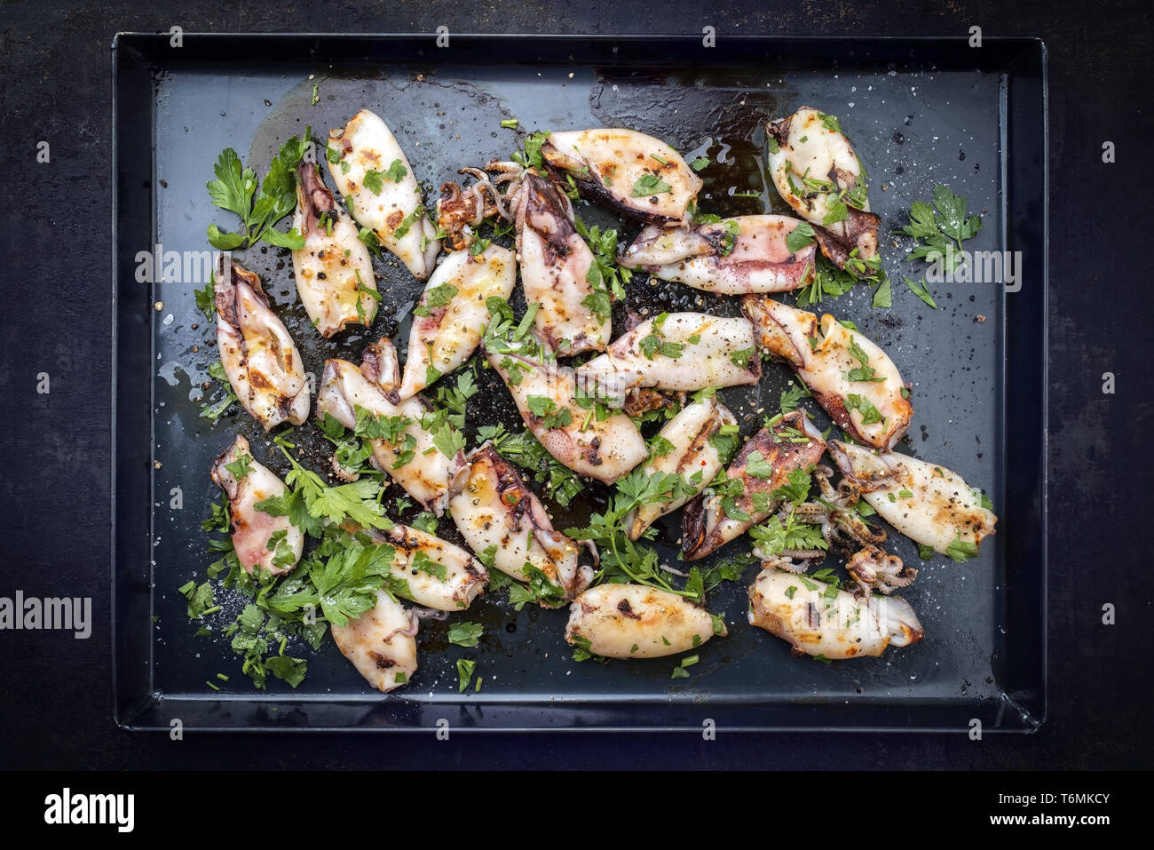 Barbecue tradizionale greco di calamari con erbe e spezie come vista dall'alto su un nero foglio di metallo Foto Stock