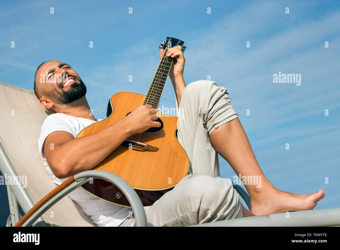 Ritratto di un uomo spagnolo con la barba e breve buzz capelli, suonando una chitarra acustica all'aperto su un cielo blu sullo sfondo. Foto Stock