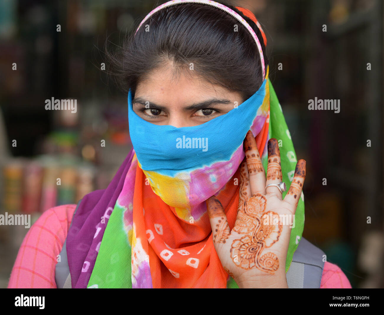 Giovani indiani del Rajasthan donna si copre la faccia con un colorato secolare velo di polvere e mostra gli intricati Henna Tattoos sulla sua sinistra palm. Foto Stock