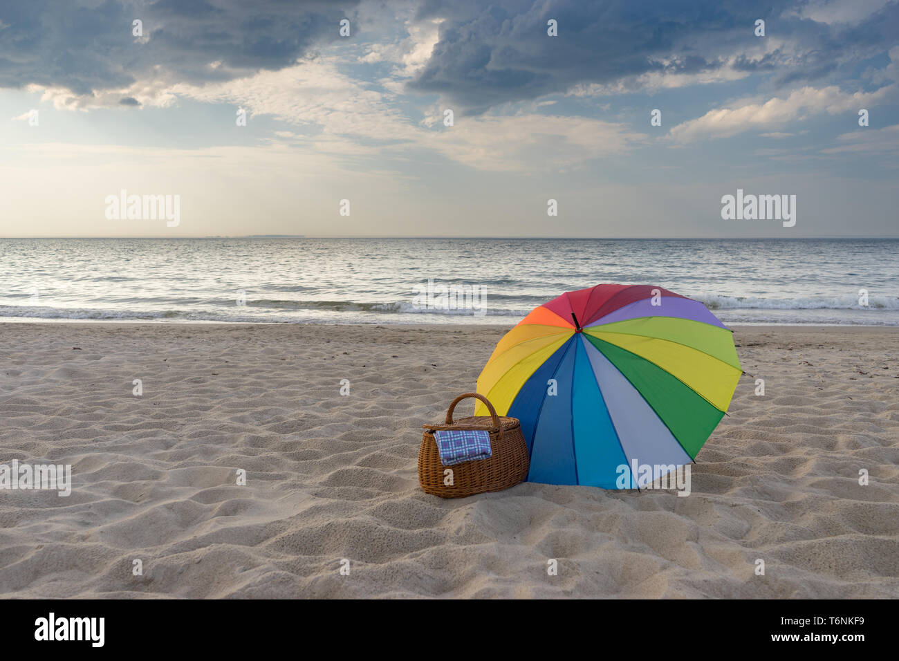Ombrello multicolore e Cesto picnic contro scenic spiaggia e mare, weekend break concept Foto Stock