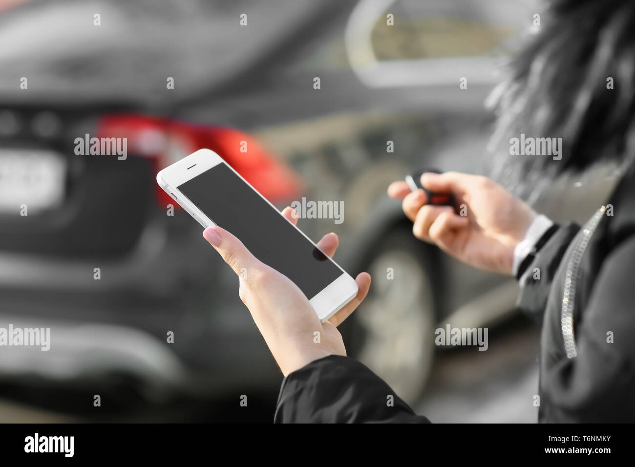 Giovane donna con il telefono utilizzando allarme auto all'aperto Foto Stock